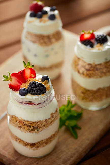 Close-up of glass jars with granola and yogurt on wooden board — Stock Photo