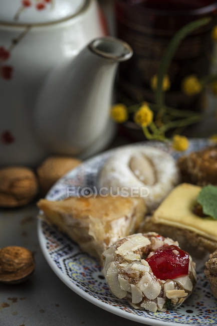 Typical Moroccan sweets with honey and almonds on plate with teapot — Stock Photo