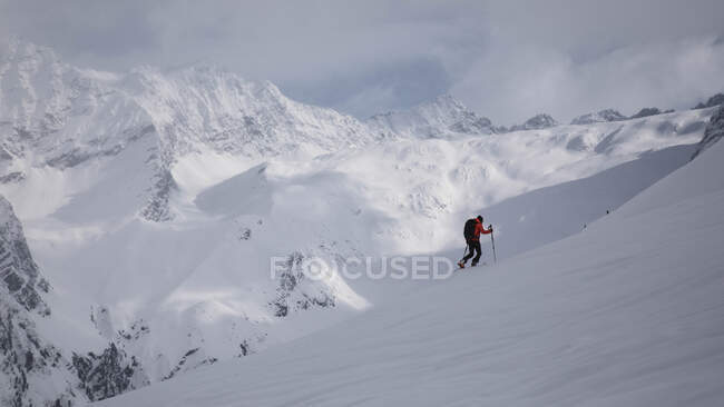 Side view of unrecognizable hiker with sticks walking up on snowy hill. — Stock Photo