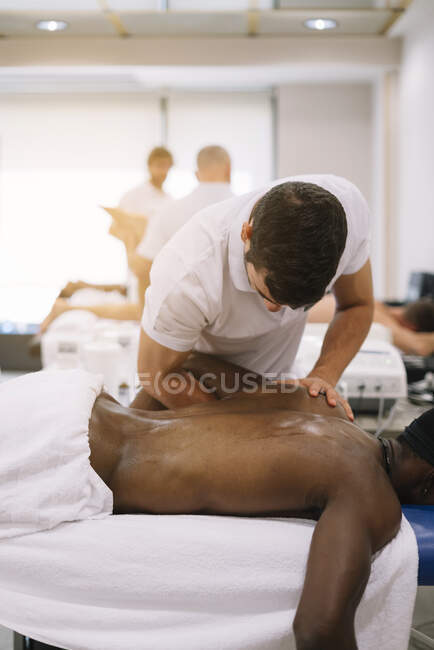 Der Physiotherapeut, der einen Mann behandelt, der Geräte für die Strahlentherapie benutzt — Stockfoto