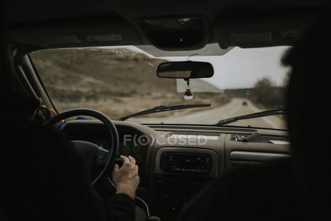 Visão traseira da pessoa irreconhecível dirigindo carro moderno ao longo da estrada rural no dia cinza — Fotografia de Stock