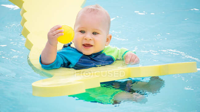 Щасливий маленький хлопчик плаває у воді з надувною іграшкою і грає з м'ячем . — стокове фото