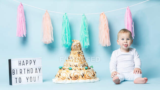 Симпатичний маленький хлопчик сидить з язиком на день народження торт на синьому фоні . — стокове фото