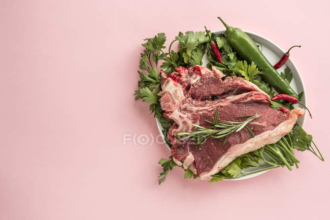 Bistecca di manzo cruda su piatto con ingredienti su sfondo rosa — Foto stock