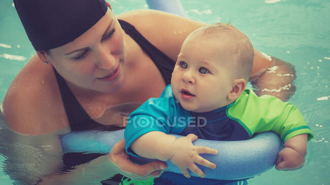 Frau mit kleinem Sohn lernt Schwimmen im Pool mit aufblasbarem Stock. — Stockfoto