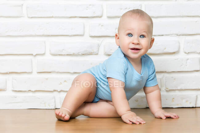 Criança olhando para a câmera e sentado no fundo da parede de tijolo branco. — Fotografia de Stock