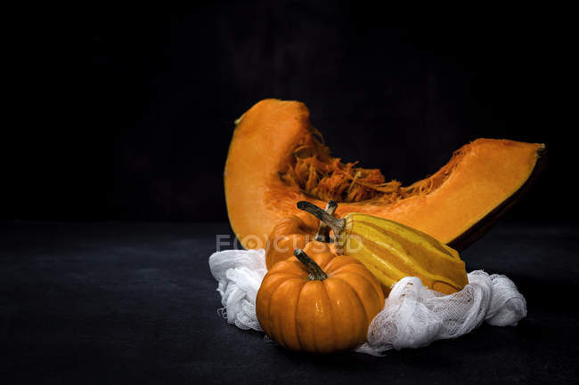 Fresh whole pumpkins with piece on white cloth on black background — Stock Photo
