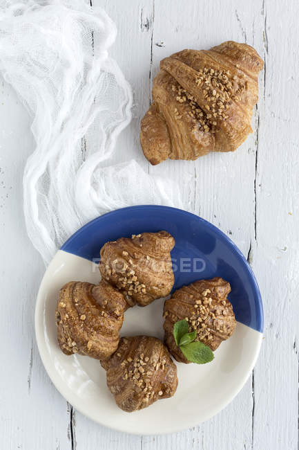 Croissant al forno su placca bianca e blu su tavola di legno con panno — Foto stock