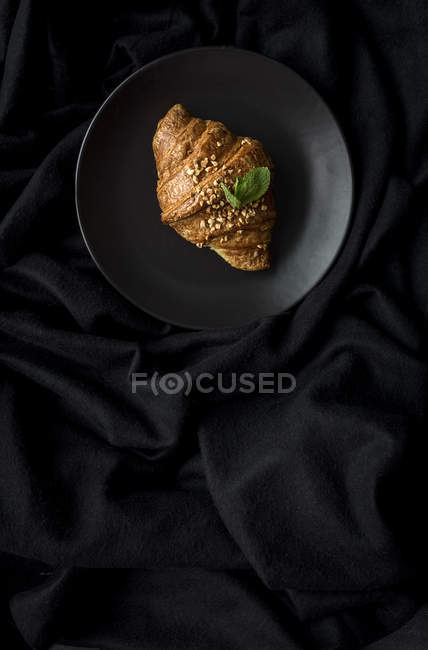 Baked croissant on plate on black fabric — Stock Photo