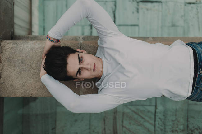 Portrait of young handsome man lying on concrete fence on street — Stock Photo