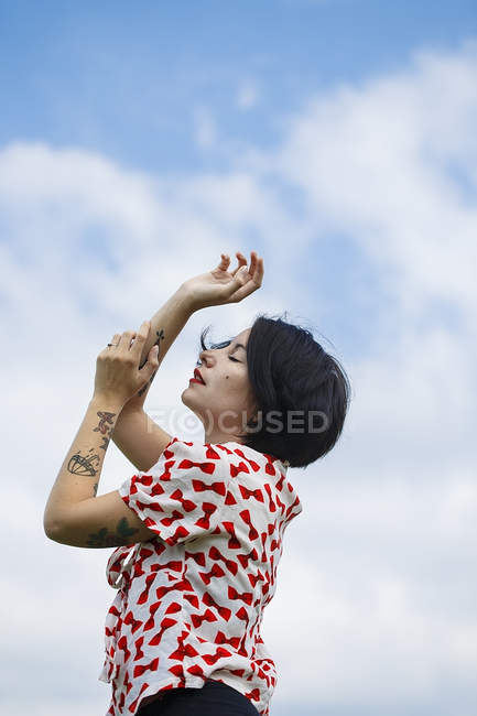 Емоційна молода жінка в візерунковому платті позує на хмарне небо — стокове фото