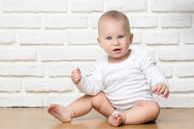 Kleines Kind blickt in die Kamera und sitzt auf dem Hintergrund einer weißen Ziegelwand. — Stockfoto
