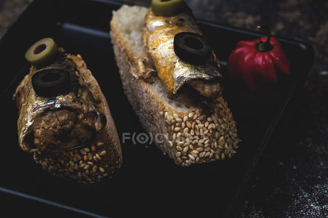 Ломтики хлеба с консервированной рыбой и оливками на сковороде рядом с горячим перцем — стоковое фото