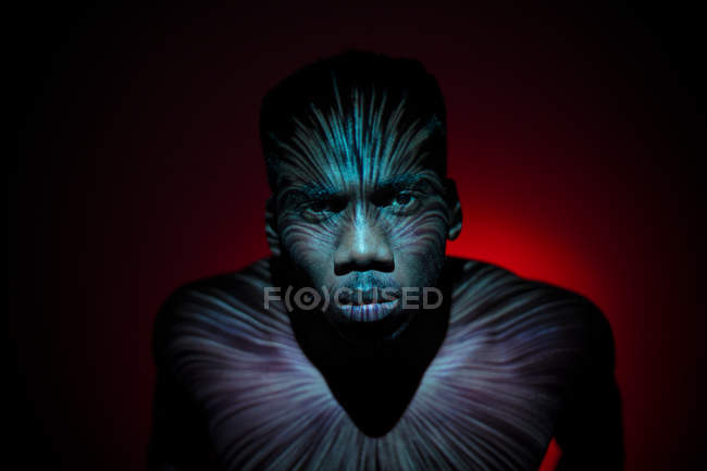 Emotionless ethnic man standing with light lines on body and looking at camera — Stock Photo