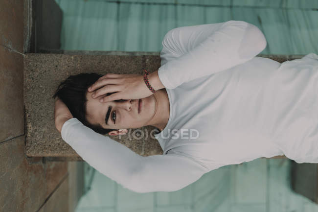 Молодой красивый мужчина лежит на бетонной стене и закрывает глаза рукой — стоковое фото