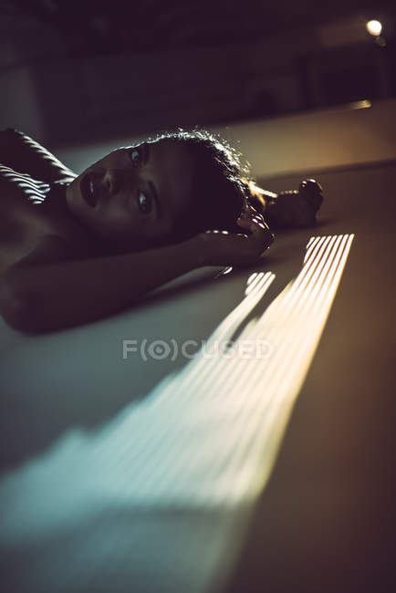Jovem mulher sedutora nua deitada em estúdio escuro e olhando para a câmera — Fotografia de Stock