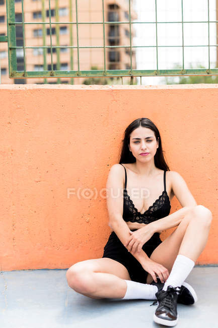 Стройная женщина в черном белье сидит на земле у бетонной стены в городе — стоковое фото
