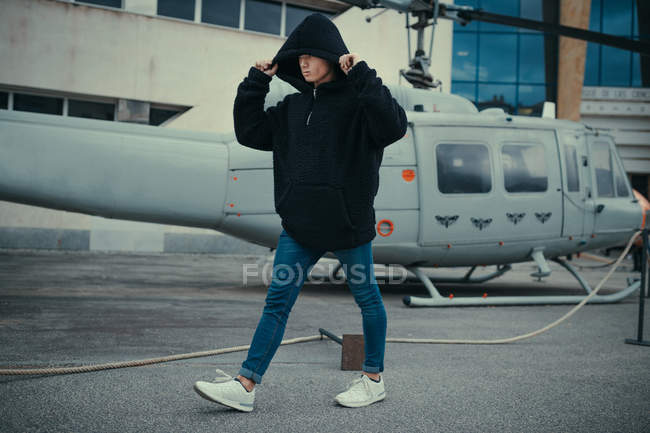 Man in black hooded jacket walking on background of helicopter monument — Stock Photo