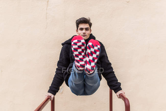 Adolescente joven haciendo ejercicio y mostrando calcetines estampados de colores en la pared beige - foto de stock