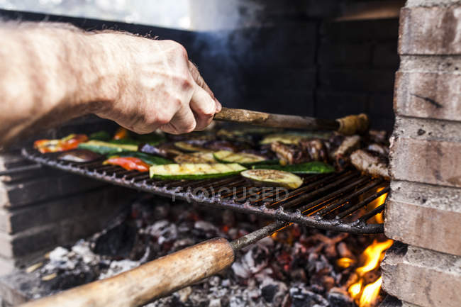 Primer plano de mano de hombre haciendo barbacoa con verduras y carne - foto de stock