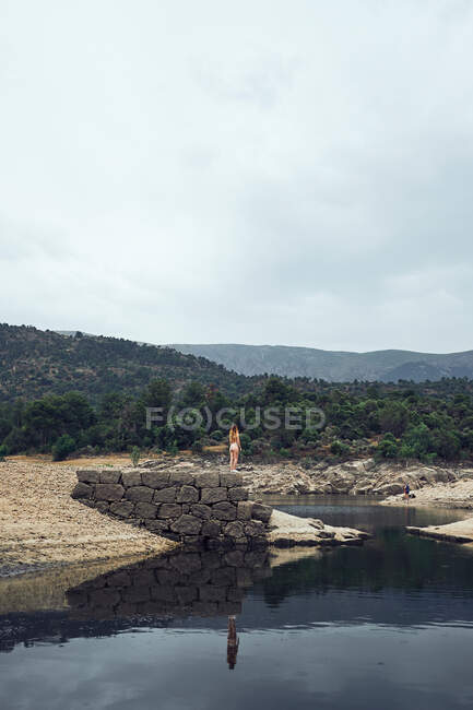 Jeune femme debout sur le rocher près de l'eau — Photo de stock