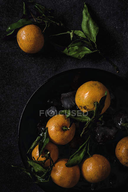Mandarini freschi maturi con foglie verdi su sfondo nero — Foto stock