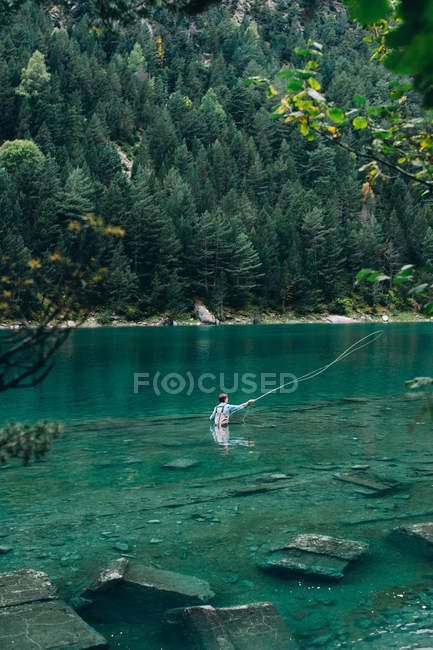 Чоловік стоїть у чистій воді мальовничого озера та риболовлі — стокове фото