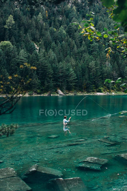 Homem de pé na água limpa do lago pitoresco e pesca — Fotografia de Stock