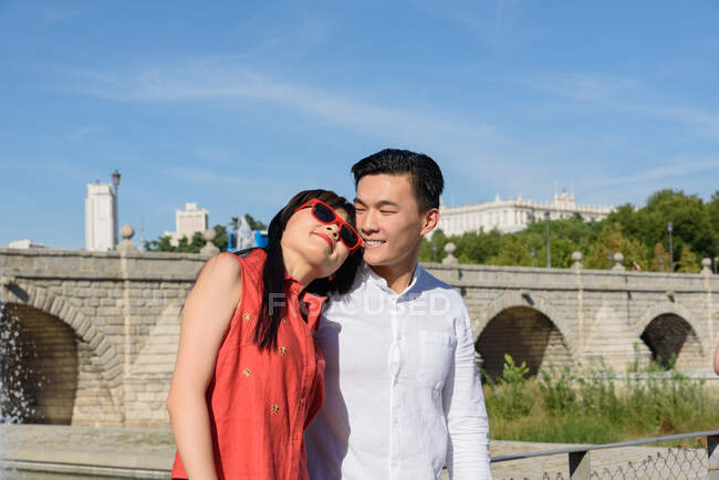 Hermosa mujer asiática apoyada en el hombro en un hombre guapo mientras están de pie en un parque increíble en un día soleado juntos - foto de stock