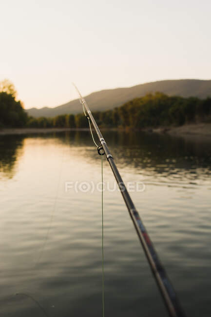Matériel de pêche long noir au-dessus de la surface tranquille de l'eau au coucher du soleil — Photo de stock