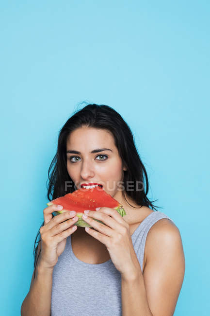 Портрет молодой женщины, поедающей арбуз на синем фоне — стоковое фото