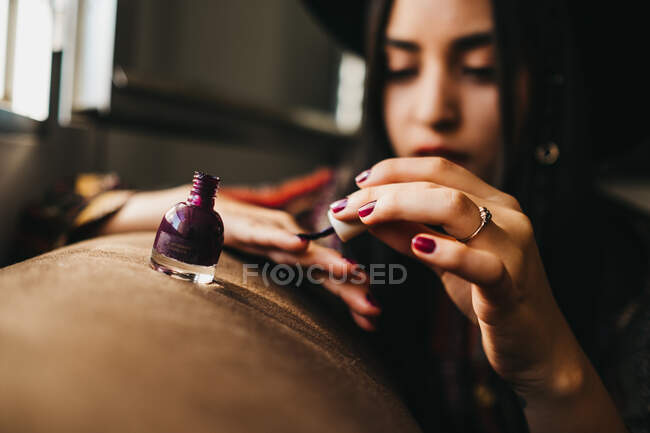 Hübsche junge Frau in stylischem Outfit mit Pinsel Nagellack auftragen, während sie auf bequemem Sofa zu Hause sitzt — Stockfoto