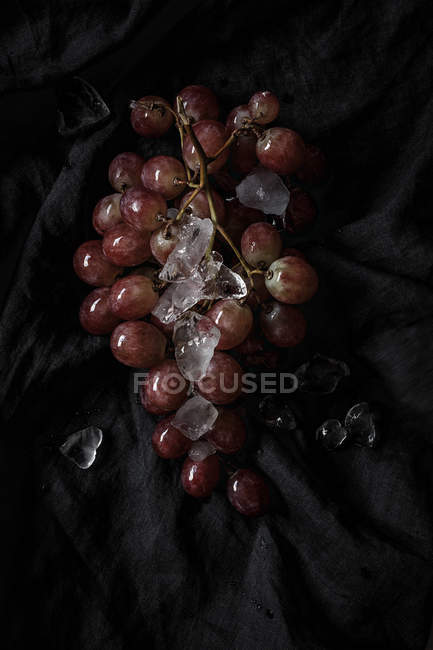 Racimo de uvas rojas frescas sobre tela negra con hielo - foto de stock