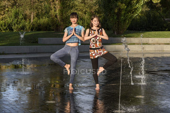 Две симпатичные азиатки, стоящие на дереве, позируют на воде современного фонтана в красивом парке — стоковое фото
