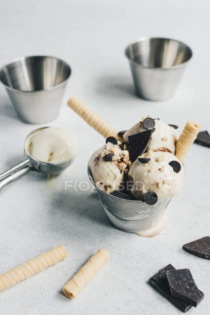Helado de vainilla con chocolate y obleas en cubo pequeño sobre mesa blanca - foto de stock