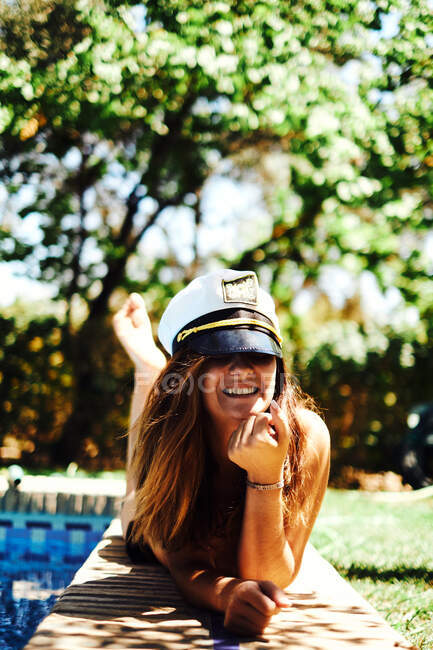 Mujer en sombrero de capitán acostada cerca de la piscina - foto de stock