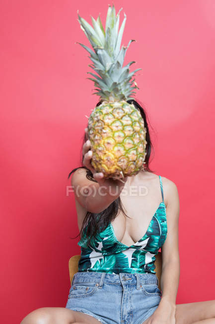 Jovem segurando abacaxi na frente do rosto no fundo rosa — Fotografia de Stock