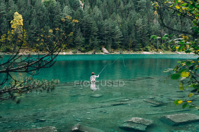 Чоловік стоїть у чистій воді мальовничого озера та риболовлі — стокове фото