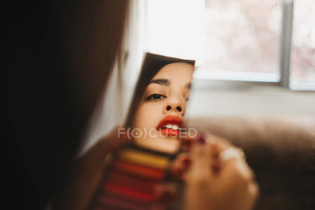 Spiegelbild einer jungen Frau, die einen Taschenspiegel hält und sich zu Hause schminkt — Stockfoto