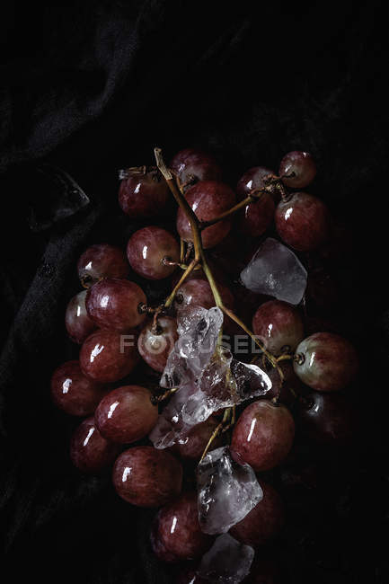 Racimo de uvas rojas frescas sobre tela negra con hielo - foto de stock