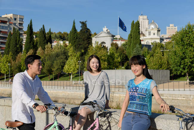 Asian man and women smiling while standing on city street near bicycles — Stock Photo