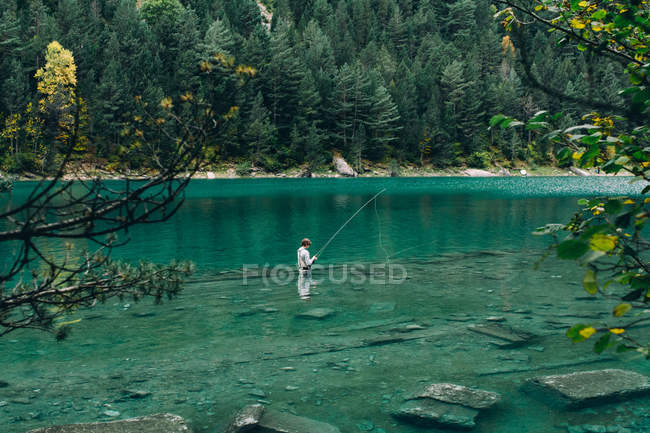 Homem de pé na água limpa do lago pitoresco e pesca — Fotografia de Stock