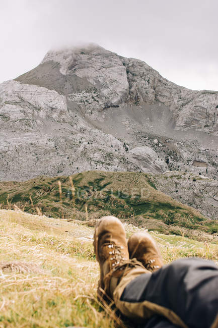 Ноги мандрівника лежать на трав'яному схилі біля величної скелі в природі — стокове фото