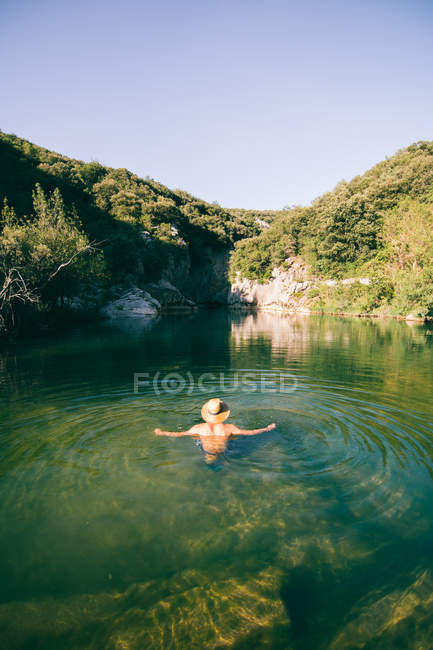Back view of shirtless guy in hat standing in clean water of amazing lake in mountains — Stock Photo
