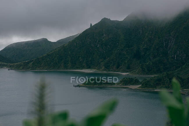 Majestuosas altas montañas con azul lago todavía en el fondo de gris cielo sombrío - foto de stock