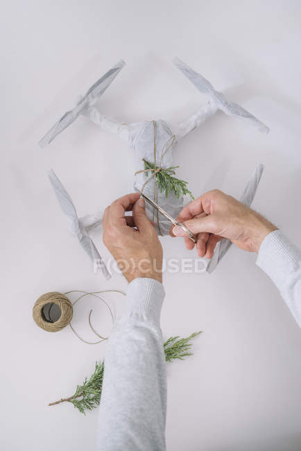 Male hands wrapping drone as Christmas gift with fir branch and twine on white background — Stock Photo