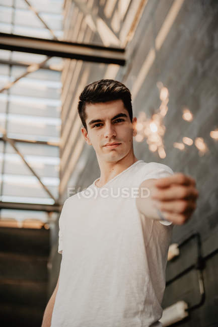 Young handsome man in white T-shirt standing inside building and holding burning Bengal light in hand — Stock Photo