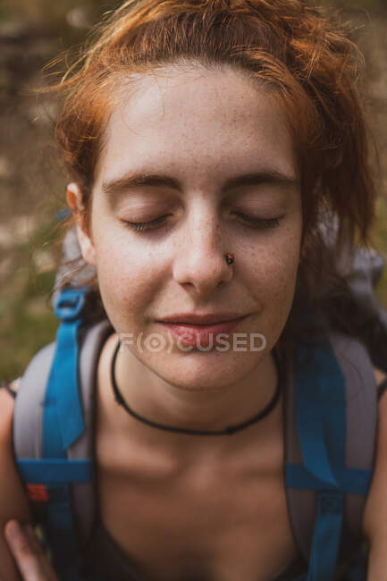 Pretty young woman with backpack smiling and squinting while standing on blurred background of nature in Bulgaria, Balkans — Stock Photo