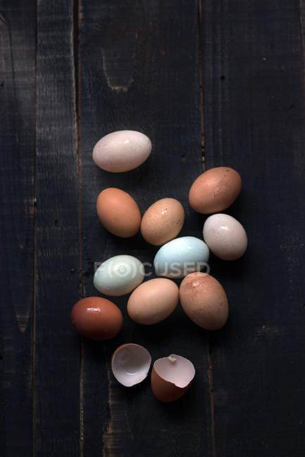 Fresh eggs on dark wooden table with eggshell — Stock Photo