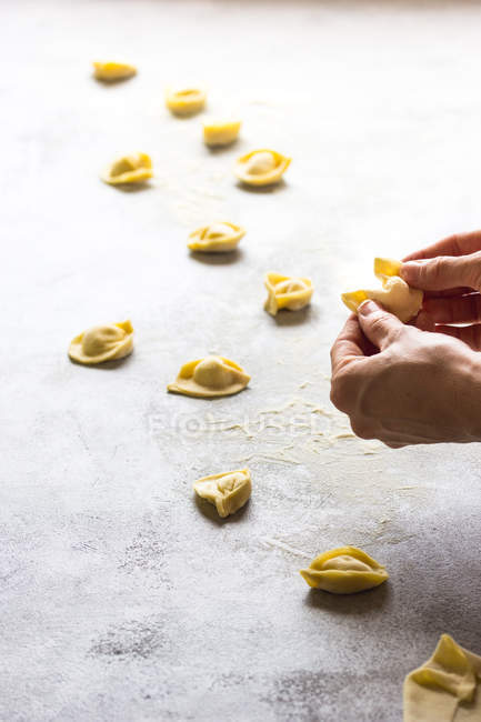 Human hands making tortellini on grey tabletop — Stock Photo